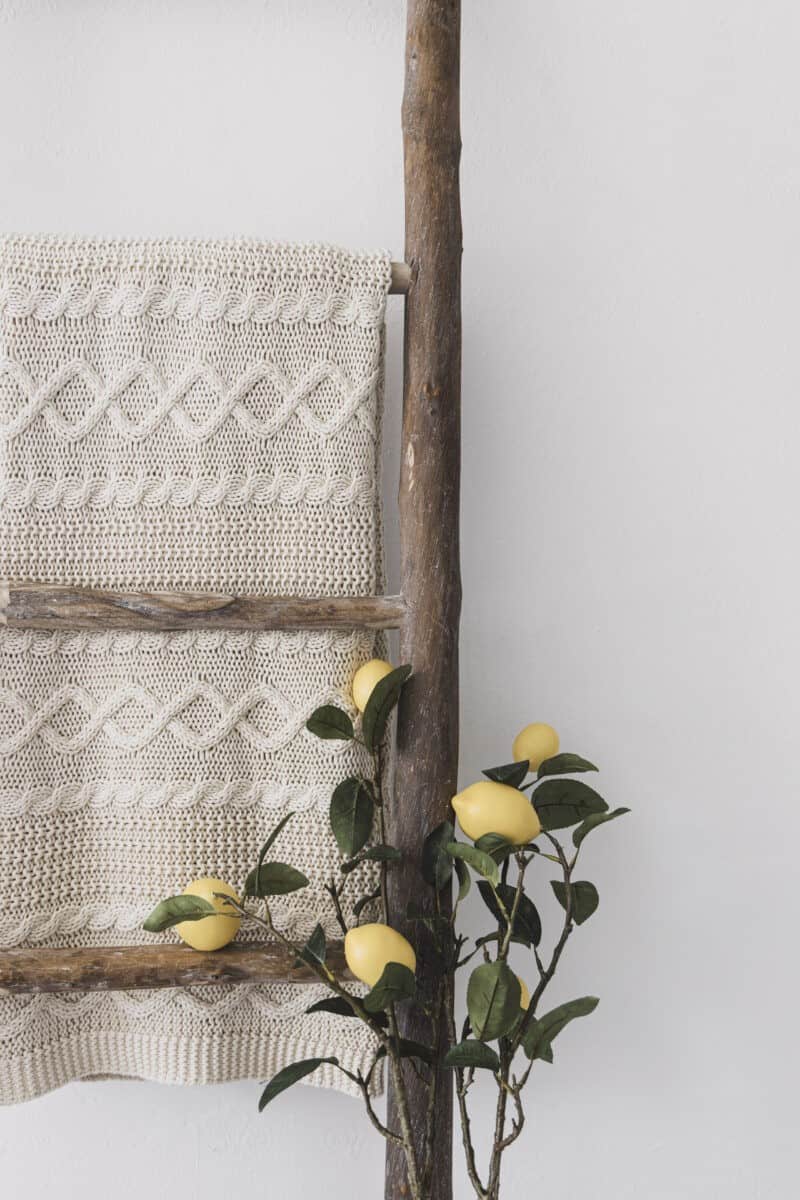 Cream knitted throw hanging over a wooden ladder with faux lemon stems. 