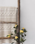 Cream knitted throw hanging over a wooden ladder with faux lemon stems. 