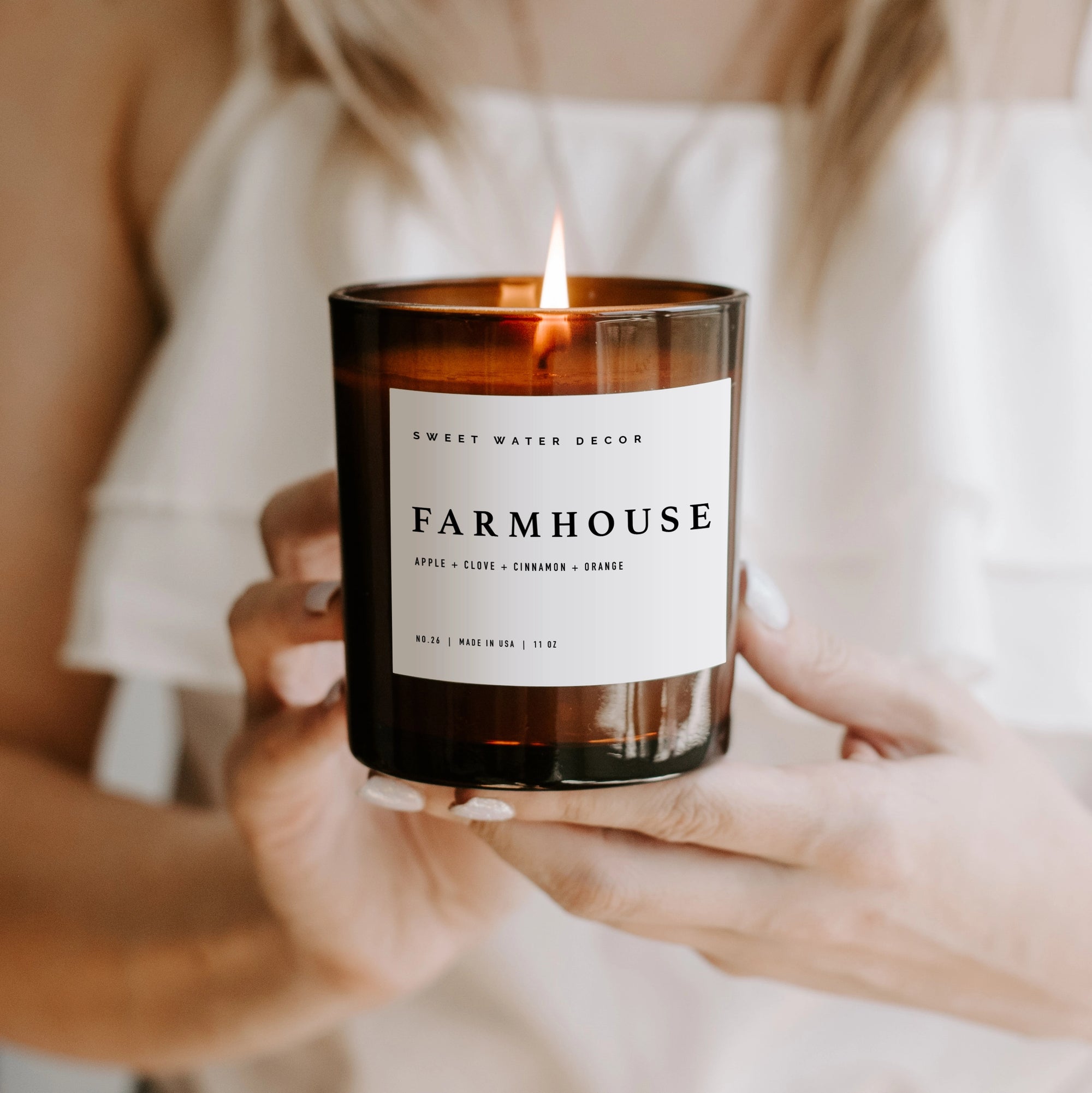 Farmhouse soy candle in amber jar, lit and held in two hands.