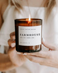 Farmhouse soy candle in amber jar, lit and held in two hands.