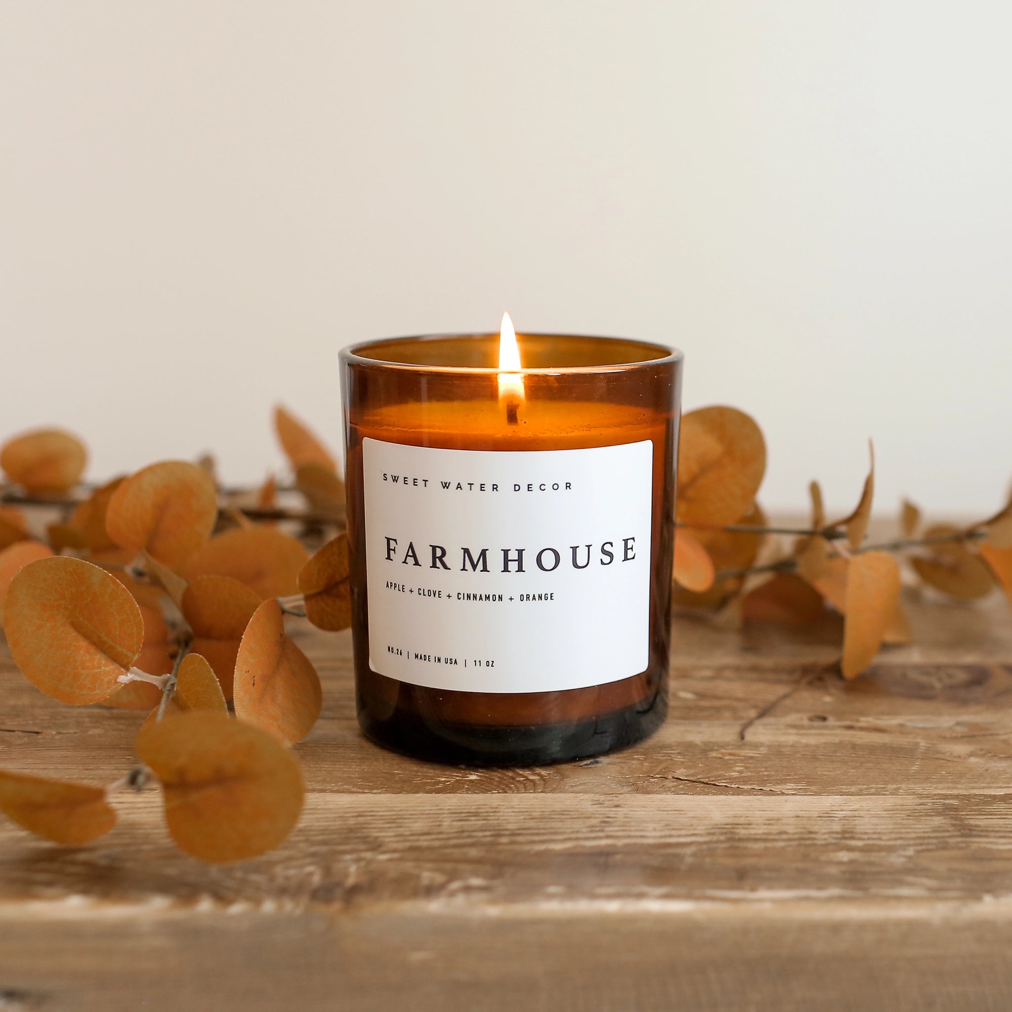 Farmhouse soy candle lit on wooden console with plants behind.