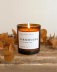 Farmhouse soy candle lit on wooden console with plants behind.