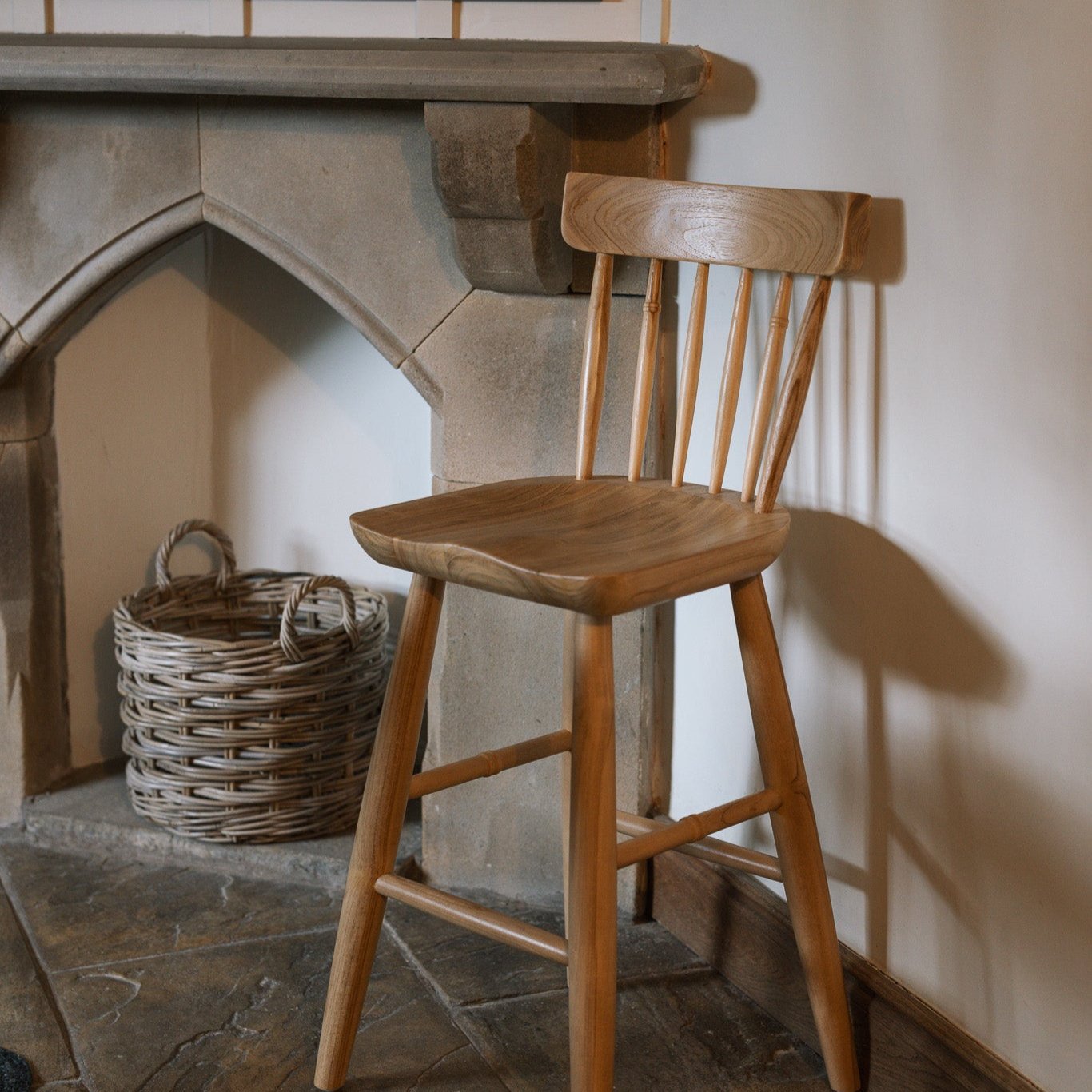 Farmhouse wooden bar stool against stone fire place on a flagged floor.