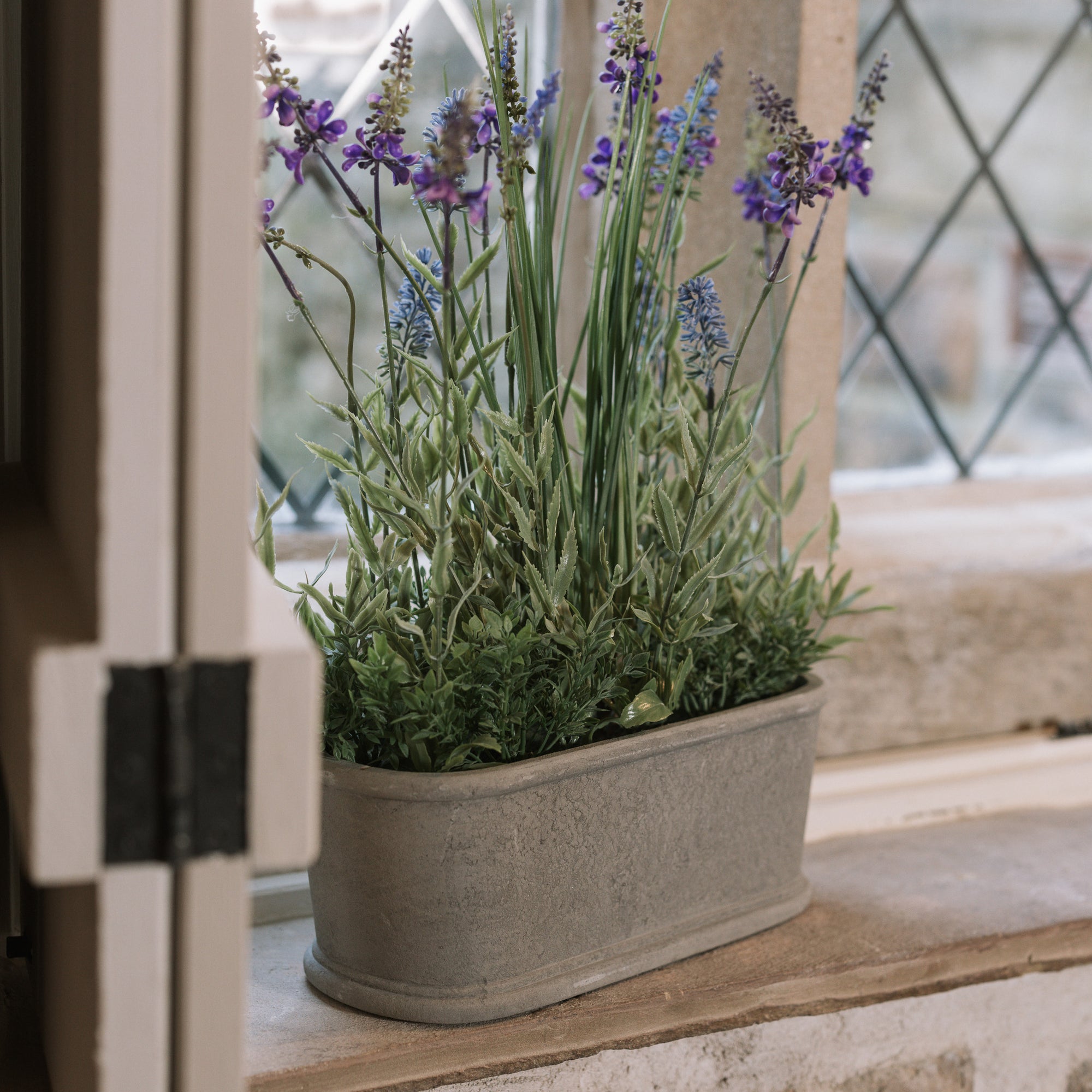 Faux lavender plant in pot on stone windowsill. 