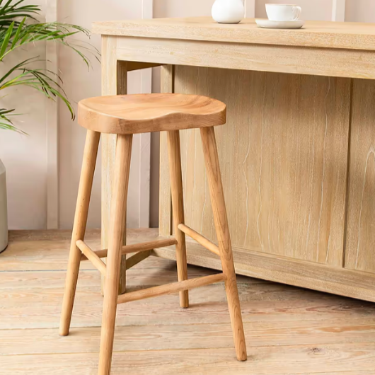 Backless wooden bat stool in front of breakfast bar with coffee cup.