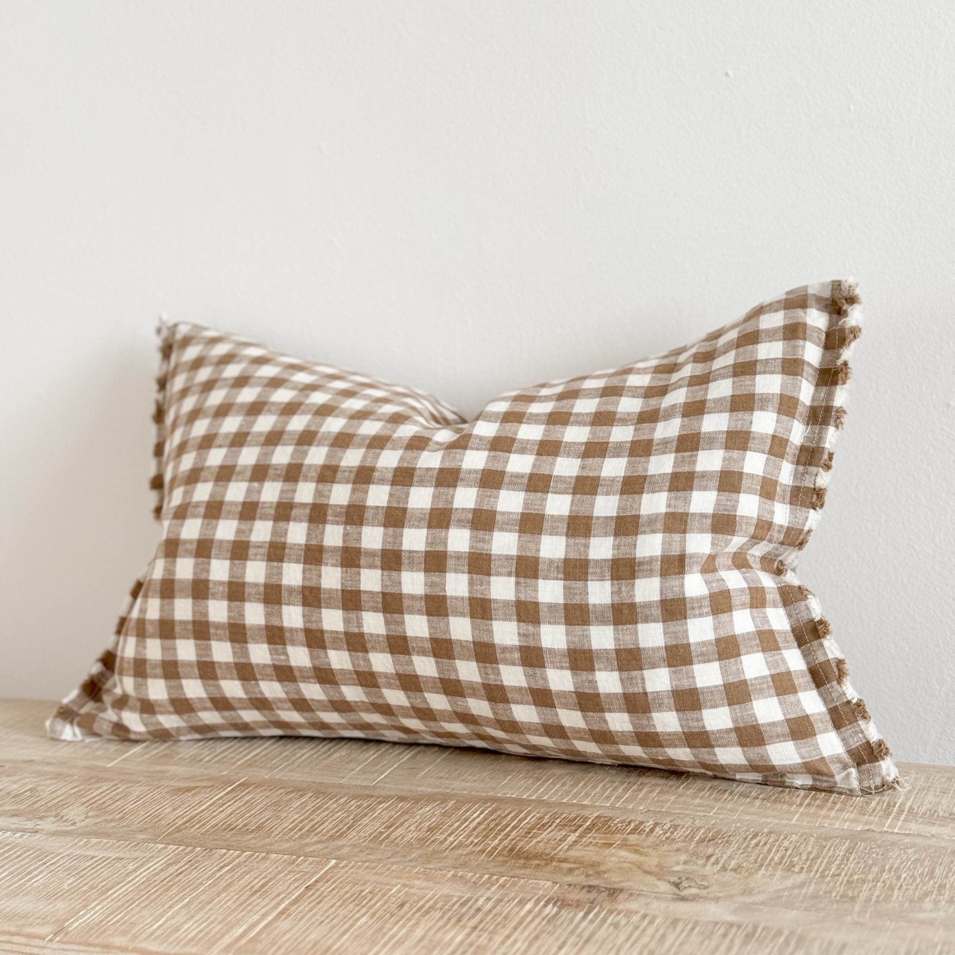 Brown and cream gingham and cream rectangle linen and cream cushion on wooden surface.