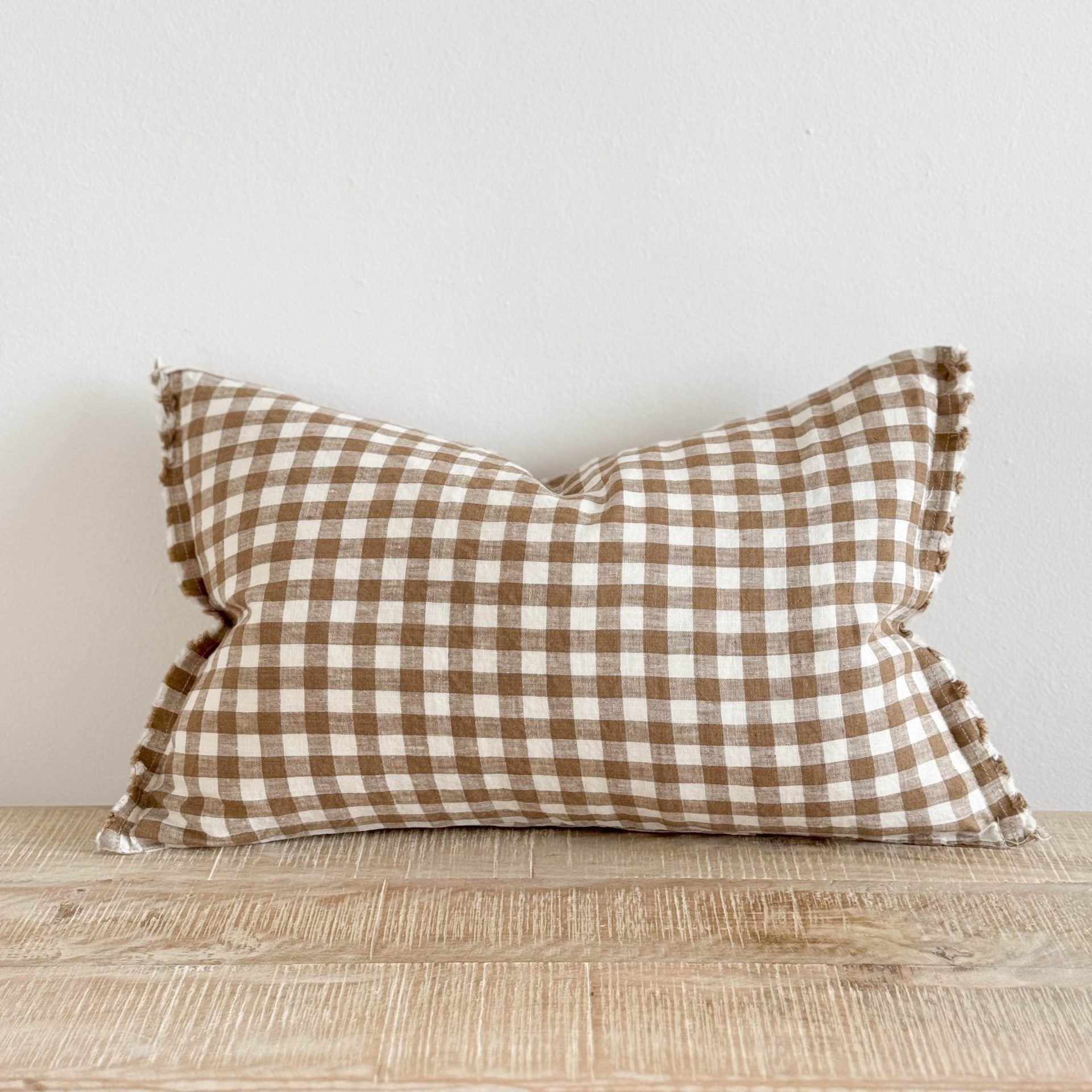 Brown and cream gingham and cream rectangle linen and cream cushion on wooden surface.