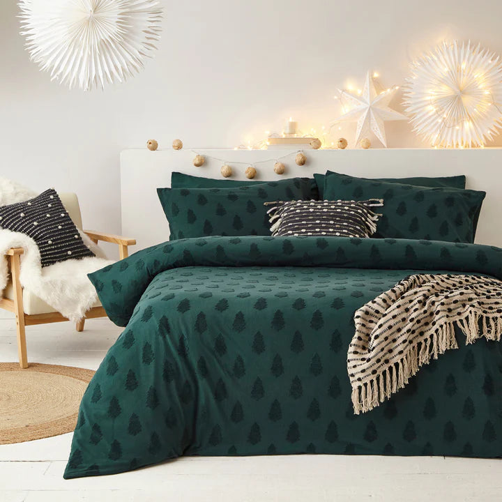 Green Christmas bedding with trees on double bed with decorations and patterned throws and cushions.