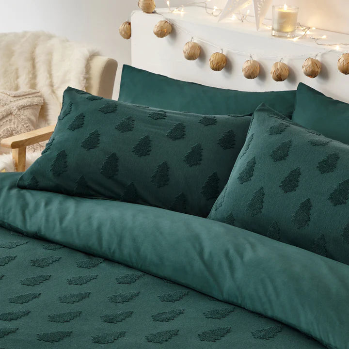 Close up of cushions on green Christmas bedding set on double bed, with Christmas garland behind.