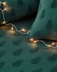 Close up of green Christmas bedding with trees, with duvet and cushions with fairy lights on top.