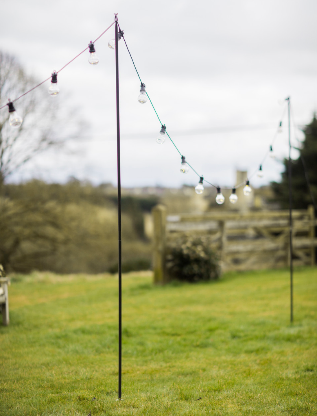 Outdoor festoon lights pole with lights on, set up in garden.