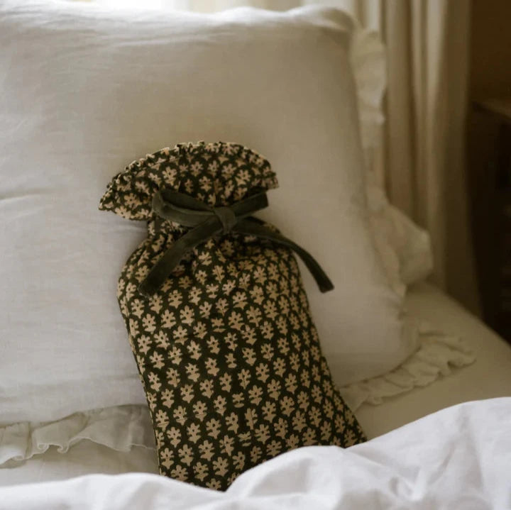 Forest green and natural hot water bottle with green bow tie closure, on white bedspread.