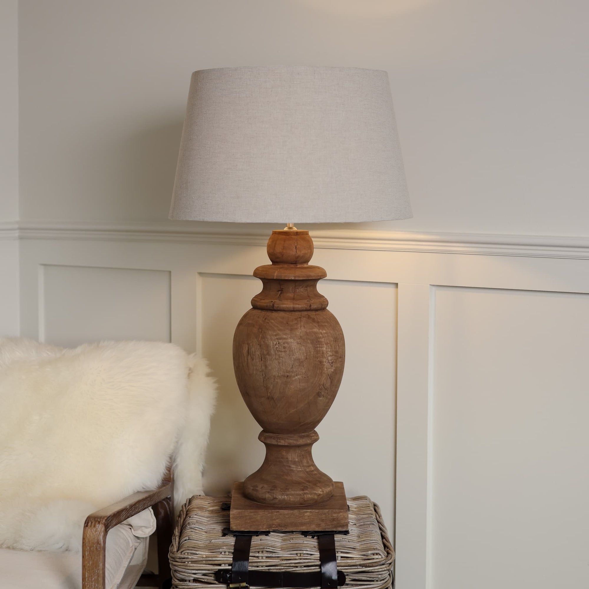 Tall wooden table lamp lit with neutral shade, lit on side table.
