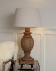 Tall wooden table lamp lit with neutral shade, lit on side table.