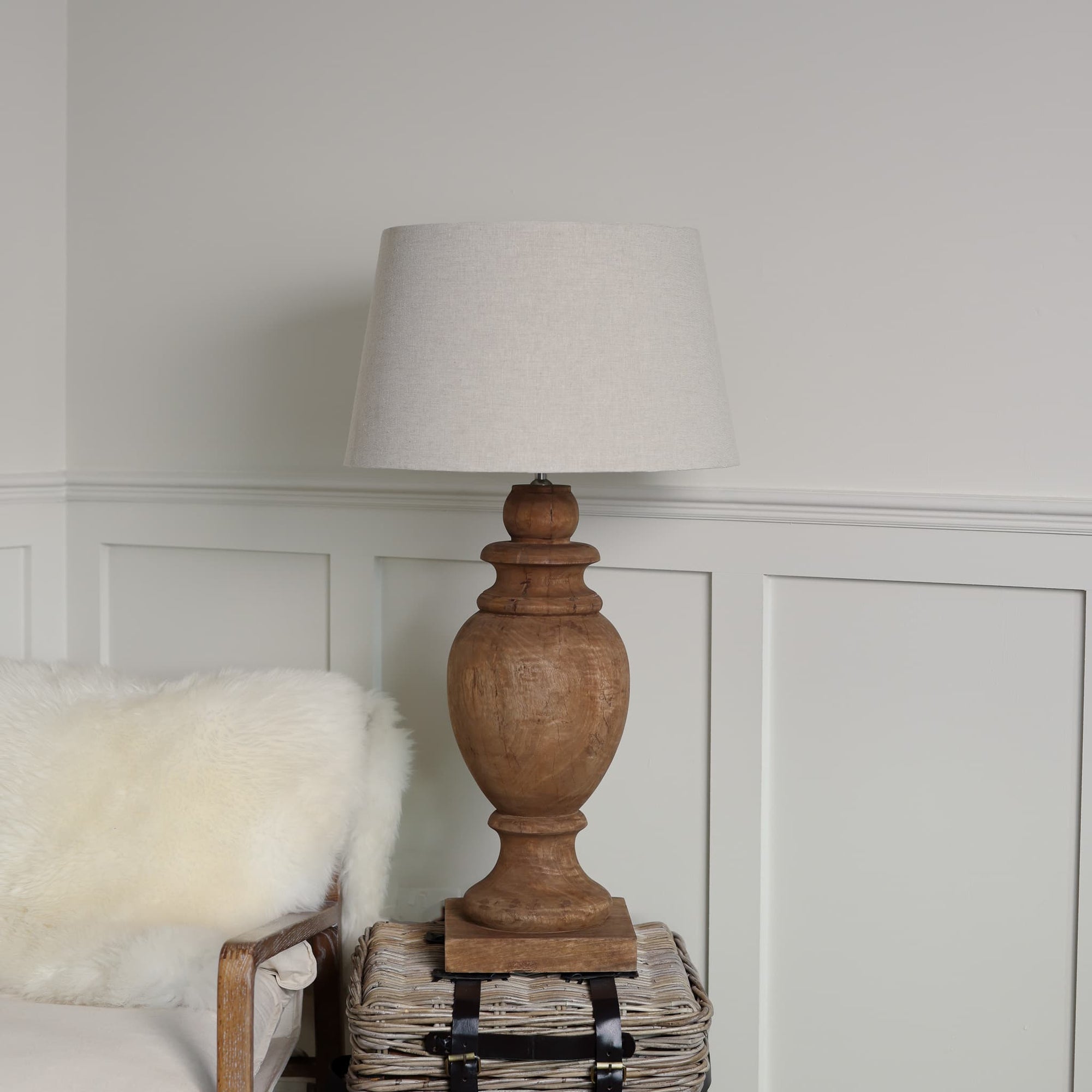 Tall wooden table lamp lit with neutral shade on side table.