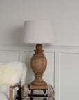 Tall wooden table lamp lit with neutral shade on side table.