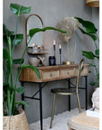 Wooden desk with drawers with rattan front and black legs with a gold chair in office.