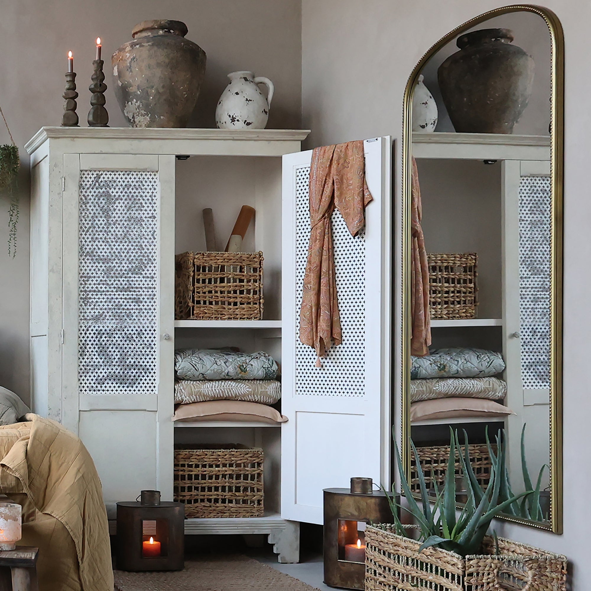 Antique cream linen closet with mesh doors, open with textiles inside.