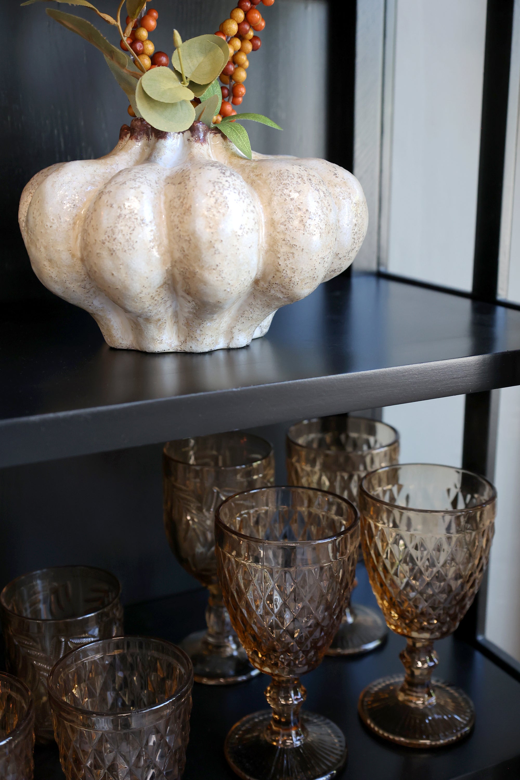 Close up of shelf on black display cabinet with amber glasses and white vase.