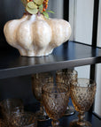 Close up of shelf on black display cabinet with amber glasses and white vase.