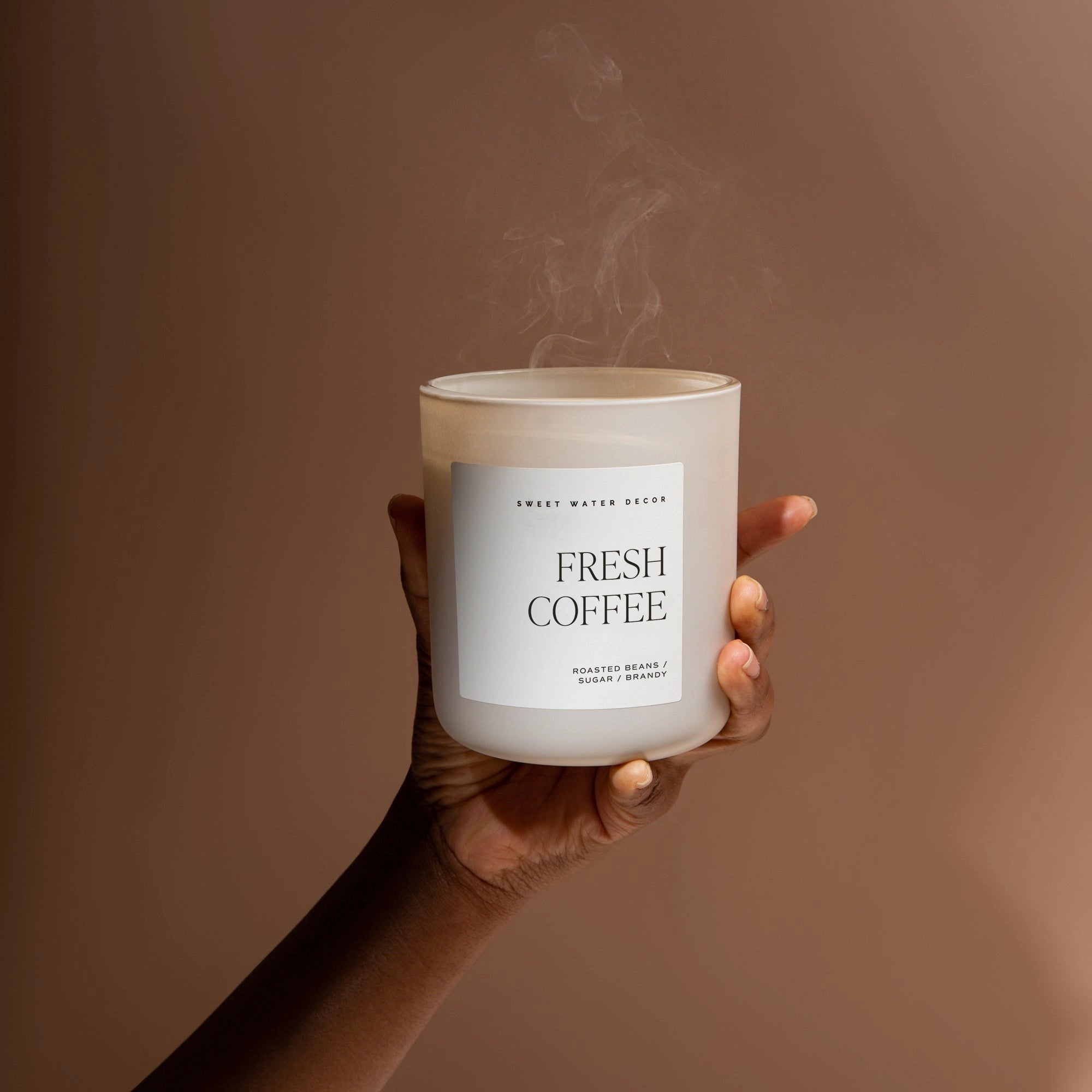 White fresh coffee soy candle in matte white jar held up with smoke blown out.