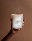 White fresh coffee soy candle in matte white jar held up with smoke blown out.