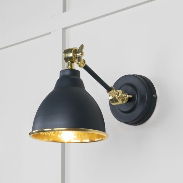 Brass and black wall light, switched on, attached to wall.