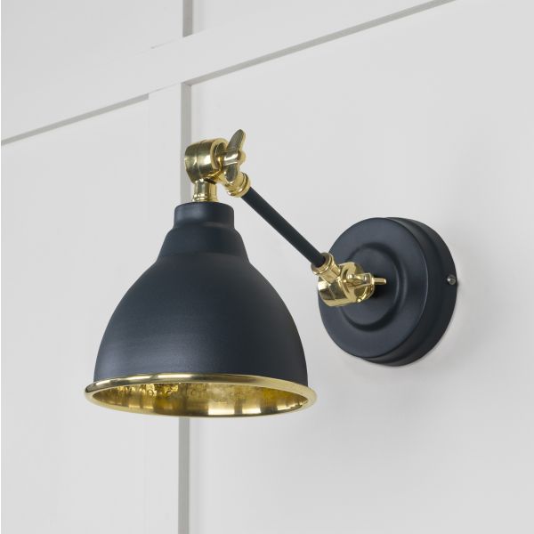 Brass and black wall light, switched off, attached to wall.