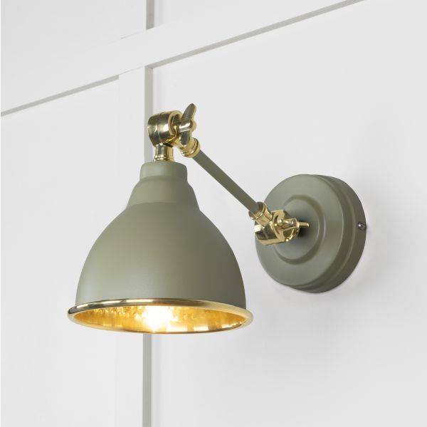 Hammered brass wall light in tump, switched on and attached to white wall.