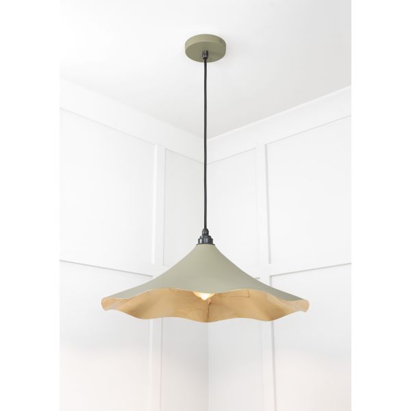 Floral brass and green pendant light, hanging from ceiling and switched on.