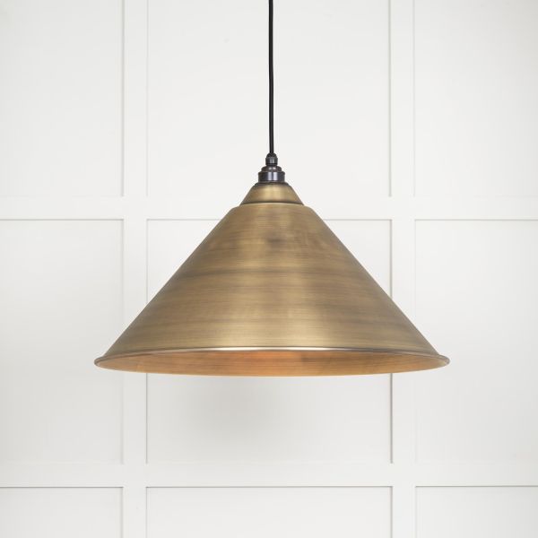 Cone shaped aged brass pendant light shade switched on.