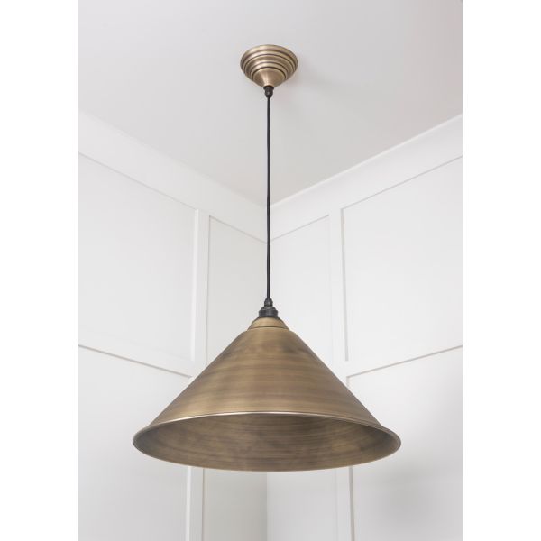 Cone shaped aged brass pendant light switched off and hanging from ceiling.