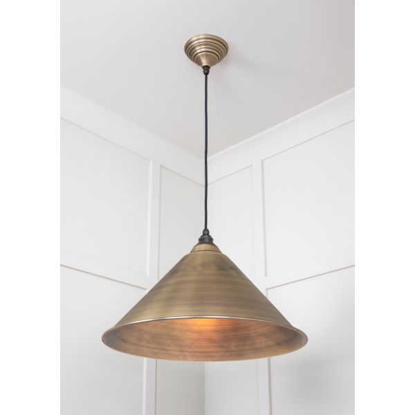 Cone shaped aged brass pendant light switched on and hanging from ceiling.