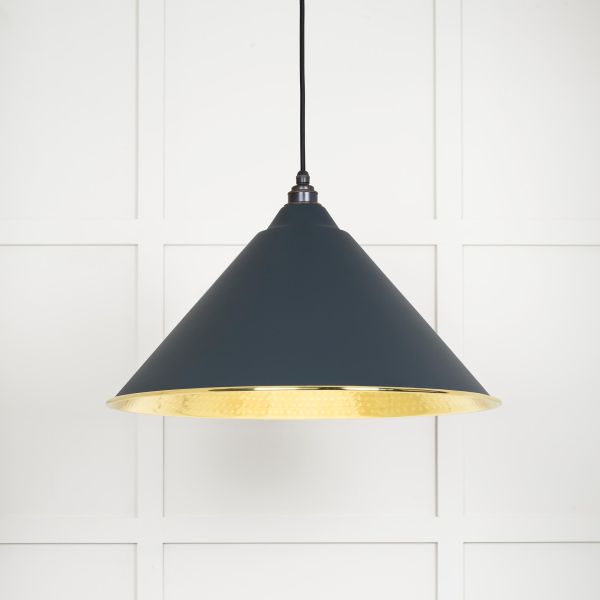 Shade on cone shaped brass and black pendant light, switched on.