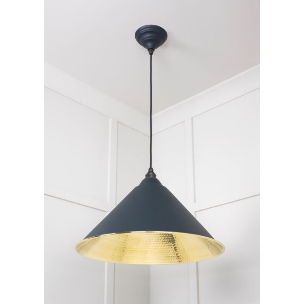 Cone shaped brass and black pendant light, switched on.