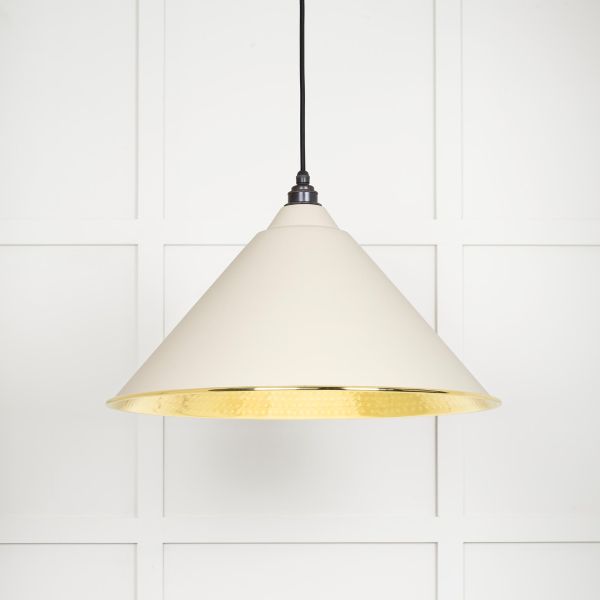 Shade of cone shaped hammered brass pendant light in teasel, switched on.