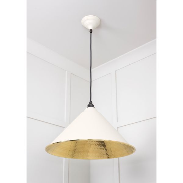 Shade of cone shaped hammered brass pendant light in teasel, switched off.