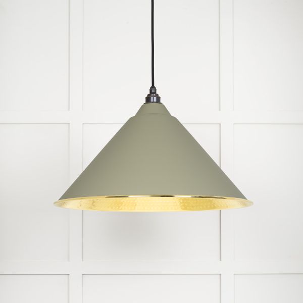 Shade of cone shaped hammered brass pendant light in green, switched on.