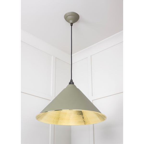 Cone shaped hammered brass pendant light in green attached to ceiling.