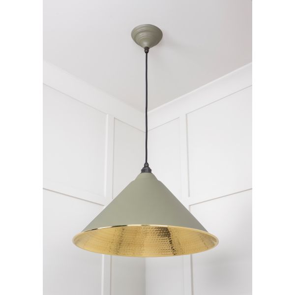 Cone shaped hammered brass pendant light in green attached to ceiling.