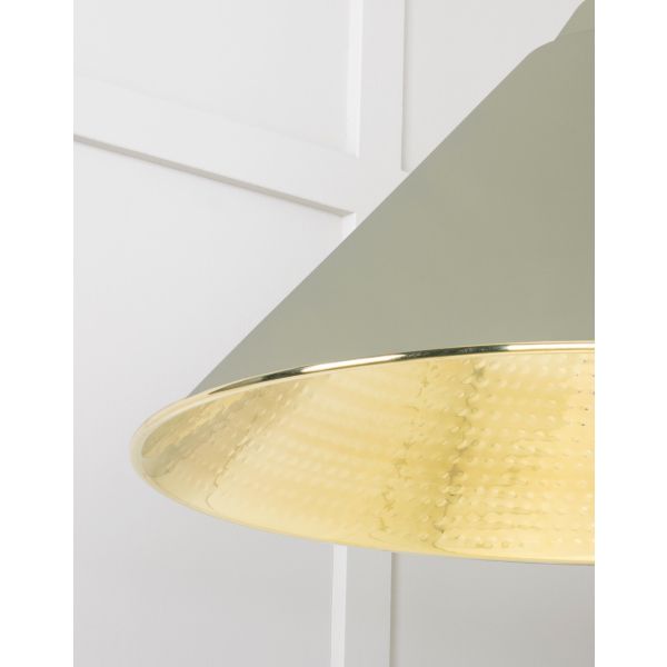 Close up of shade on cone shaped hammered brass pendant light in green attached to ceiling.