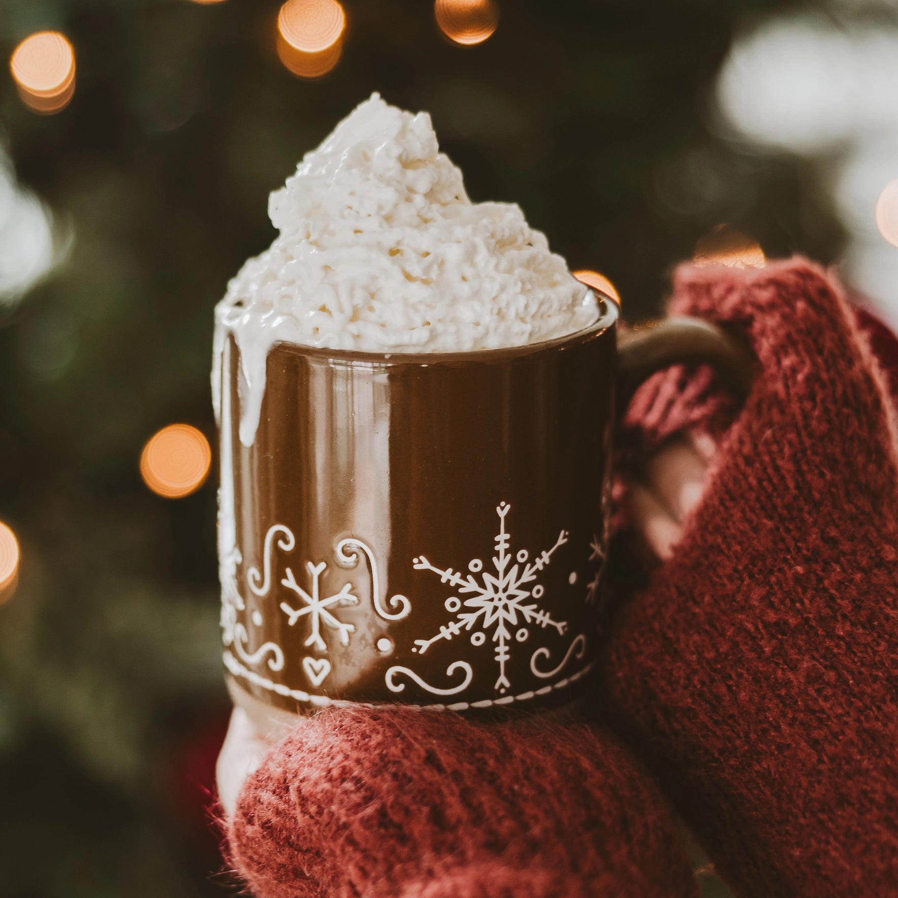 Gingerbread stoneware mug filled with whipped cream, and held with two hands. Close up of red sleeves.