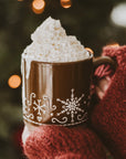 Gingerbread stoneware mug filled with whipped cream, and held with two hands. Close up of red sleeves.