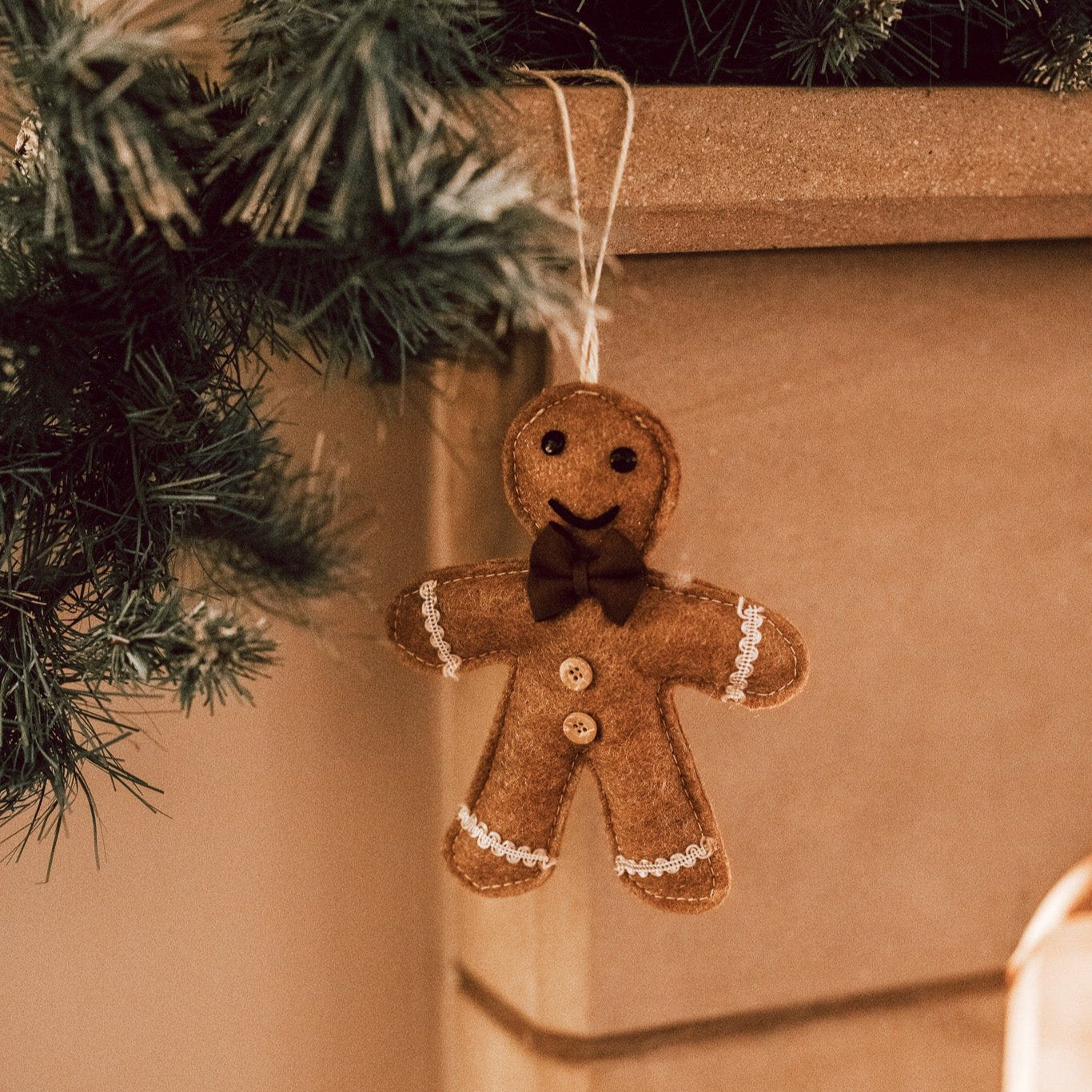 Brown hanging gingerbread Christmas decoration with bow tie and smiley face on stone mantle place with green Christmas garland.