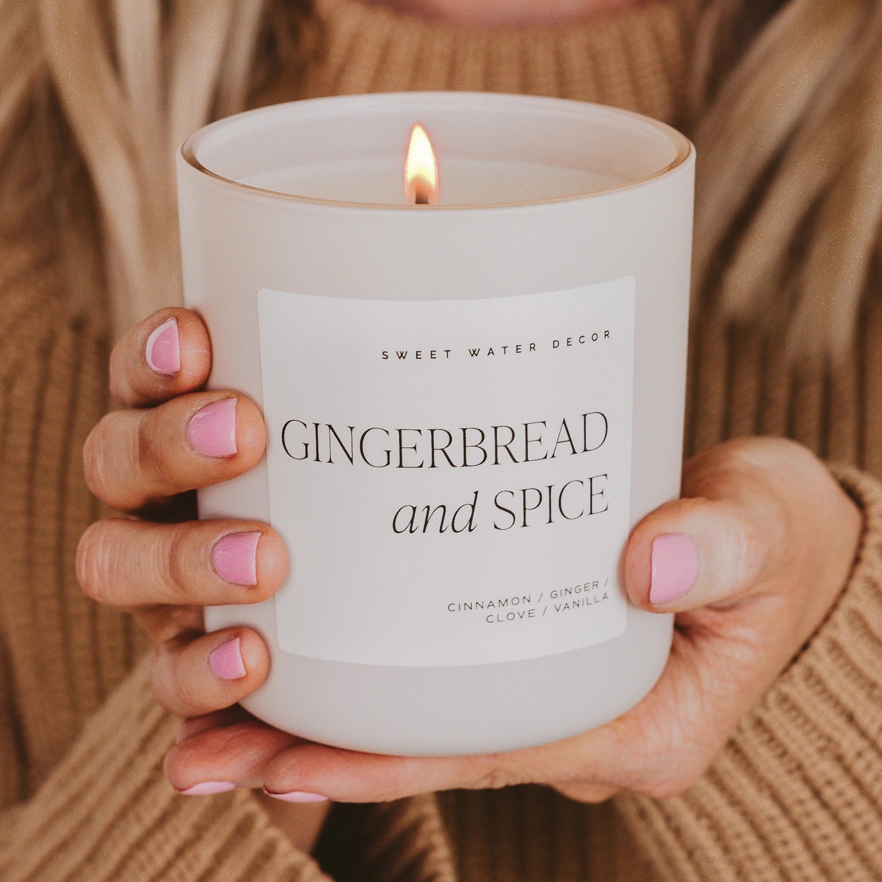 Soy candle in white jar, lit and being held up with two hands.