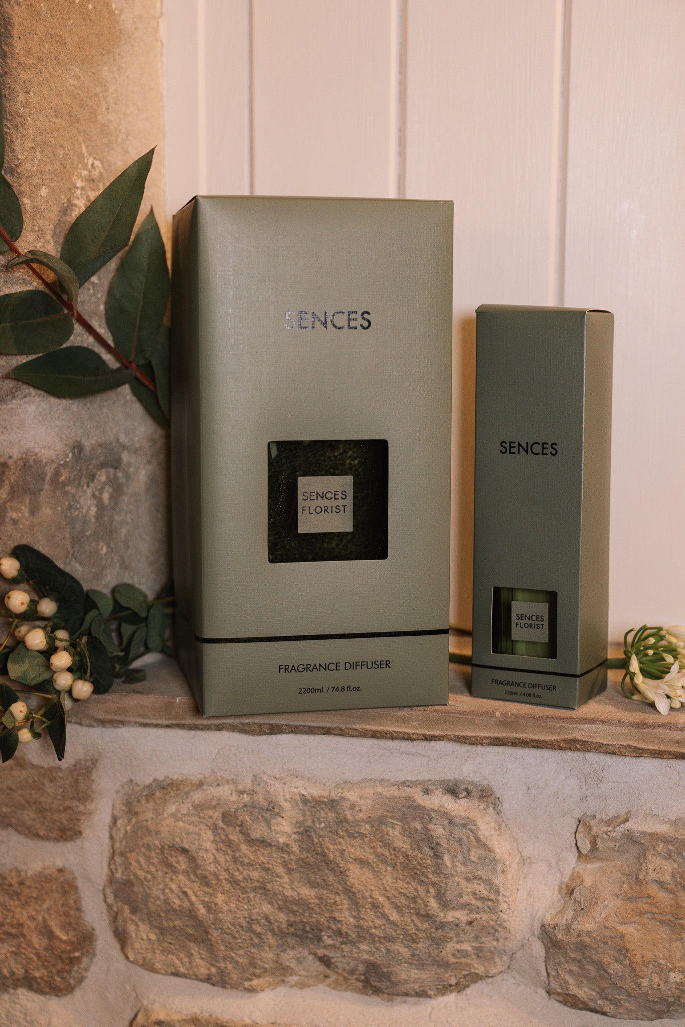 Green florist Sences reed diffuser with presentation boxes on stone windowsill.