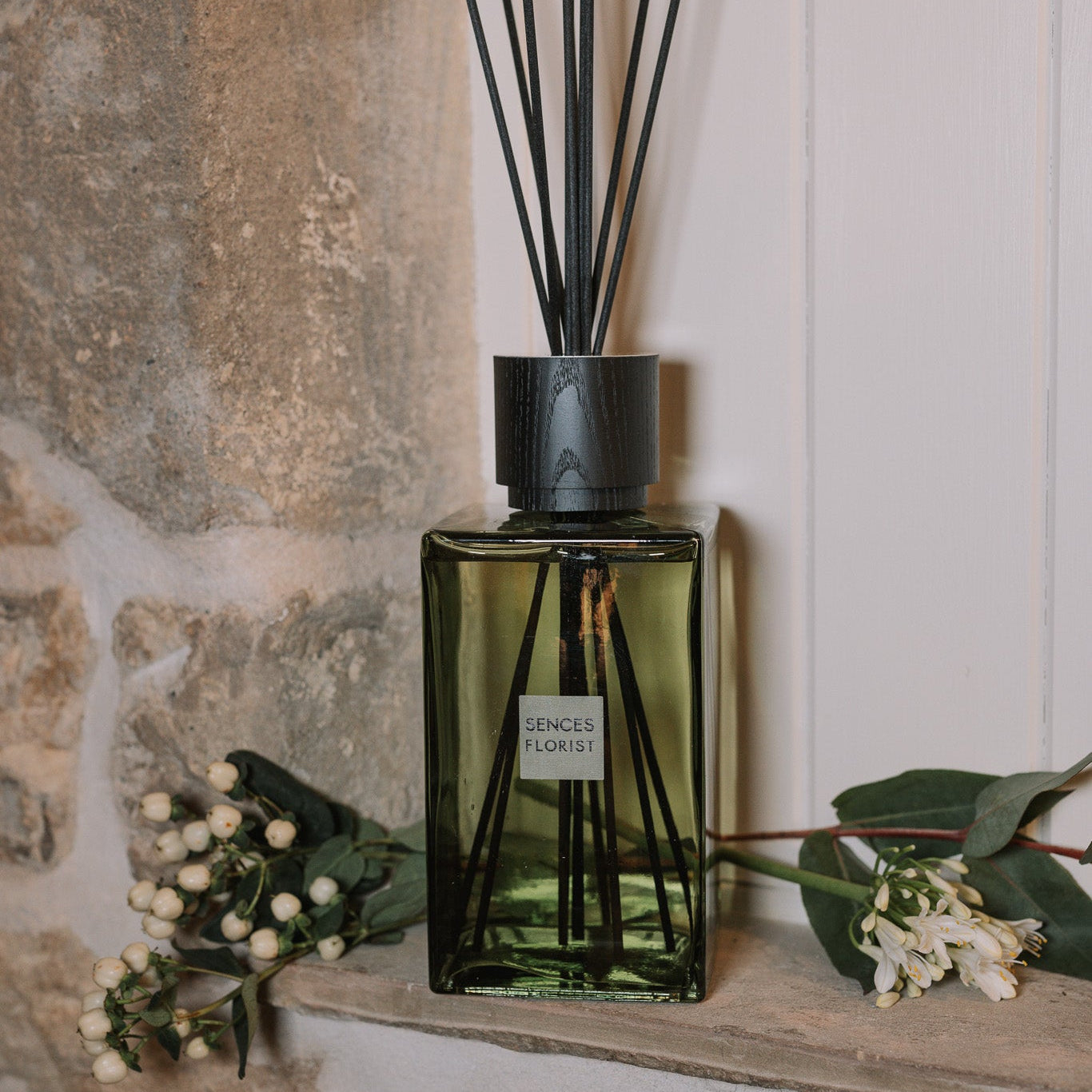 Green florist Sences reed diffuser on stone windowsill with flowers.