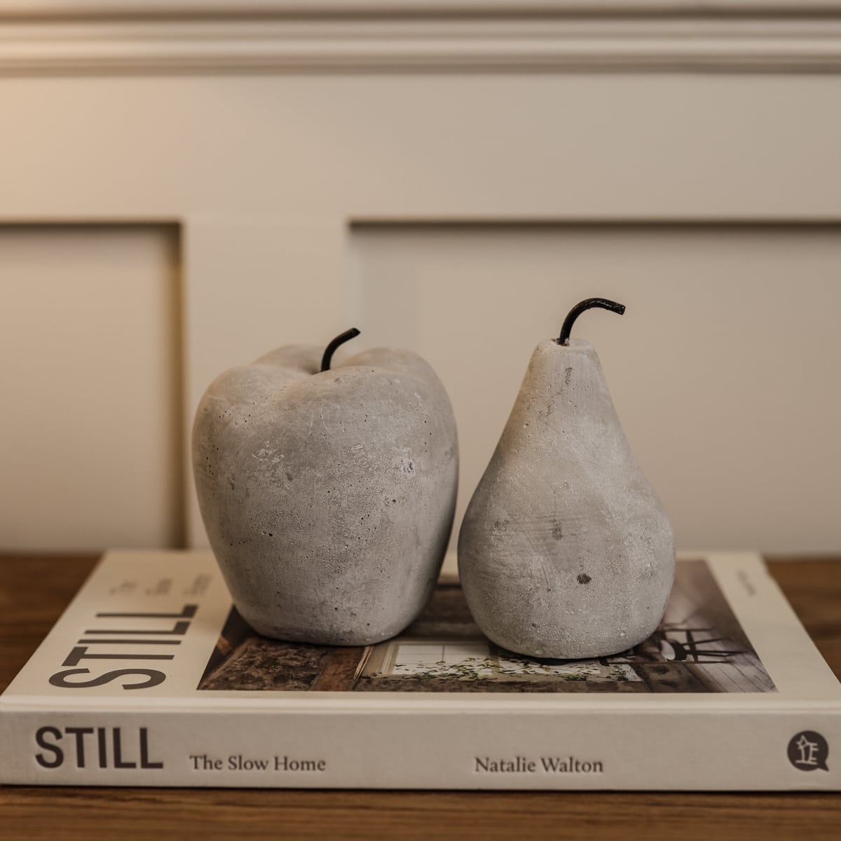 Cement grey washed apple and pear ornaments on white decorative book on wooden console.