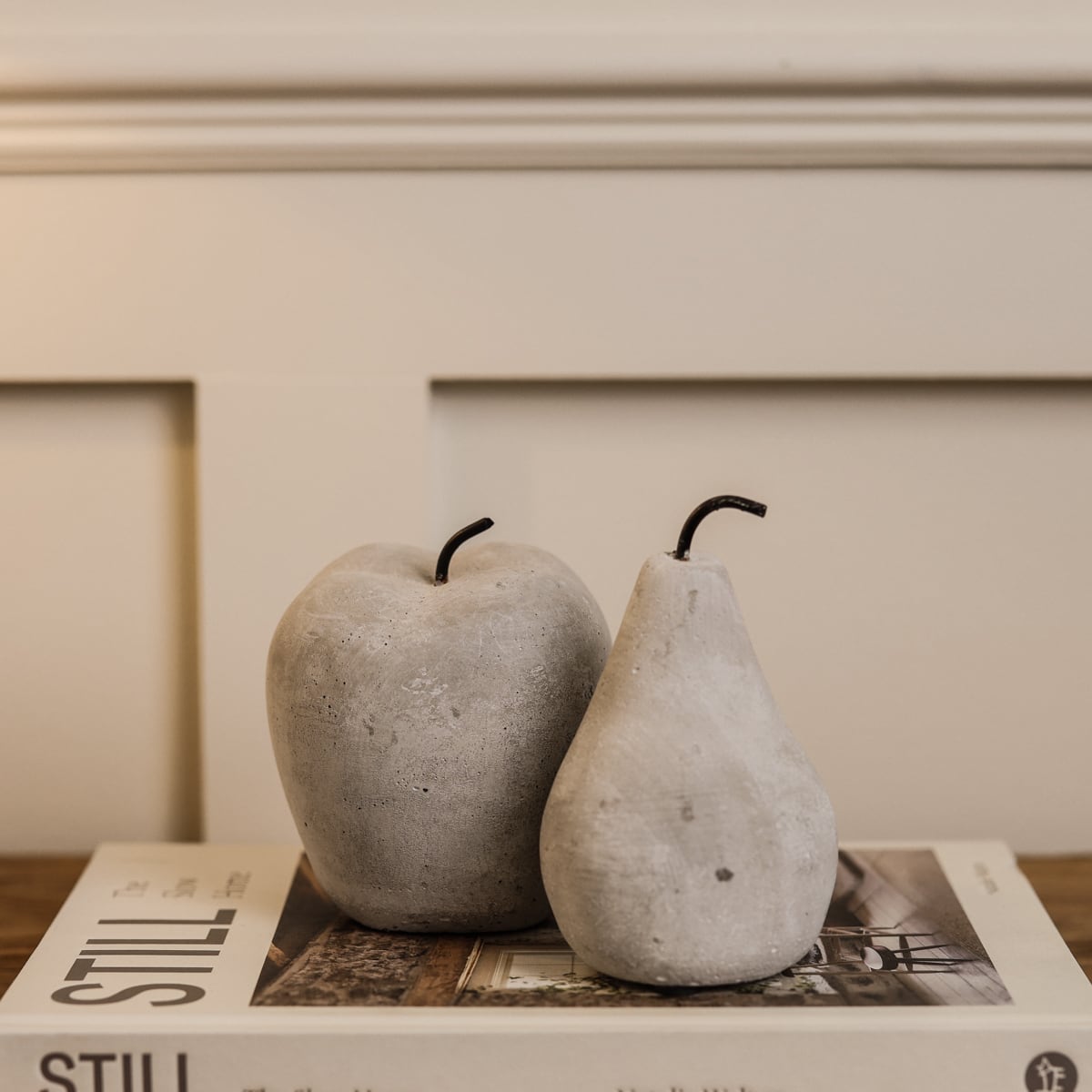 Cement grey washed apple and pear ornaments layered on white decorative book on wooden console.