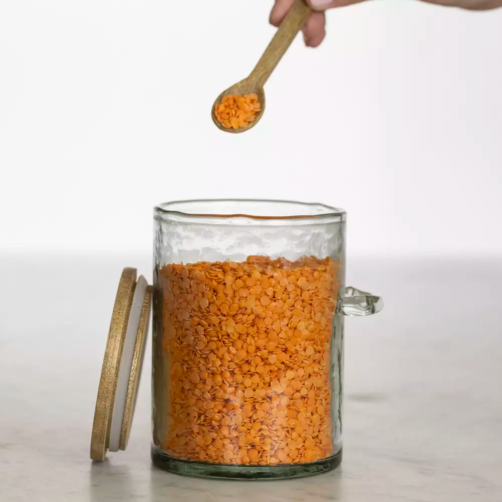 Hammered glass storage jar filled with red lentils with wooden lid and spoon.